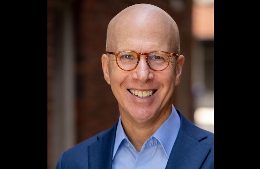  Jonathan, a white man who is bald, wears glasses and a navy suit coat with light blue button up shirt.