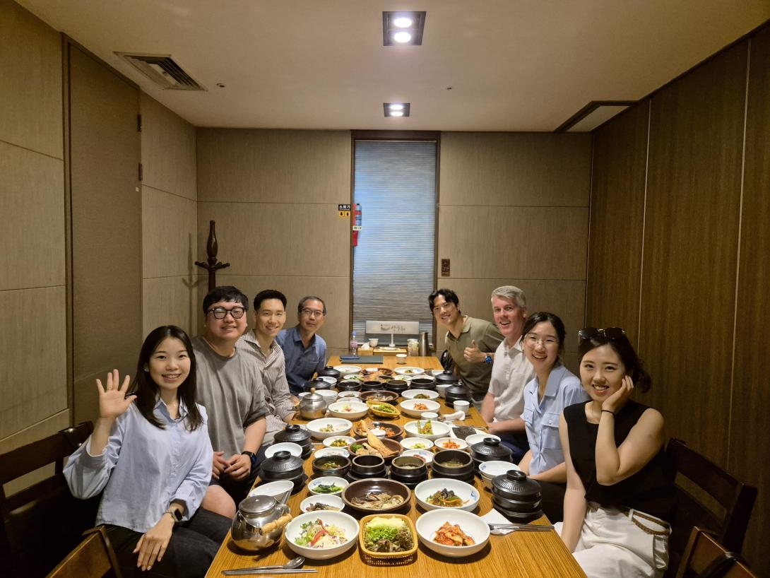 Seven Calvin alumni gathered around a dinner table, with one waving at the camera