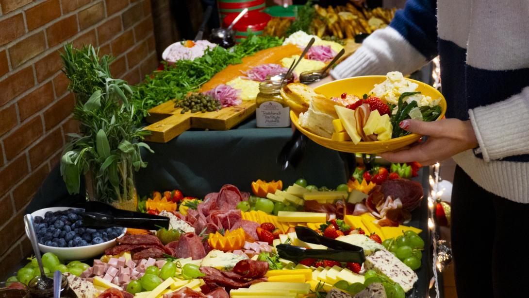 Person holding a yellow plate grabbing food from a charcuterie-grazing table.