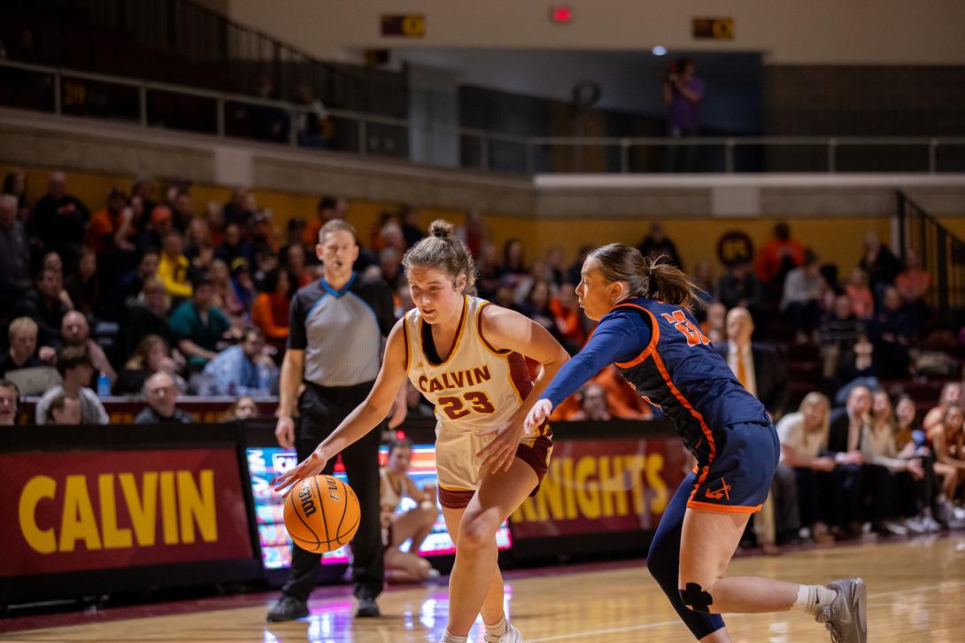 A Calvin women's basketball player dribbles down the court with a Hope College defender.