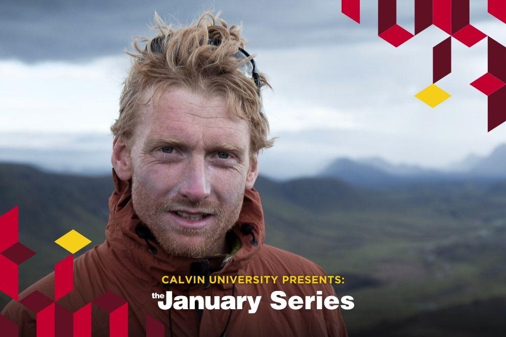 Alastair, a white man with red hair blowing in the wind, wears a red jacket with mountains in the backdrop.