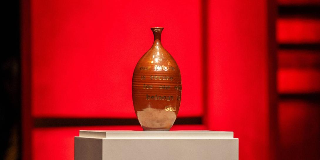 A maroon vase with gold lettering on it.