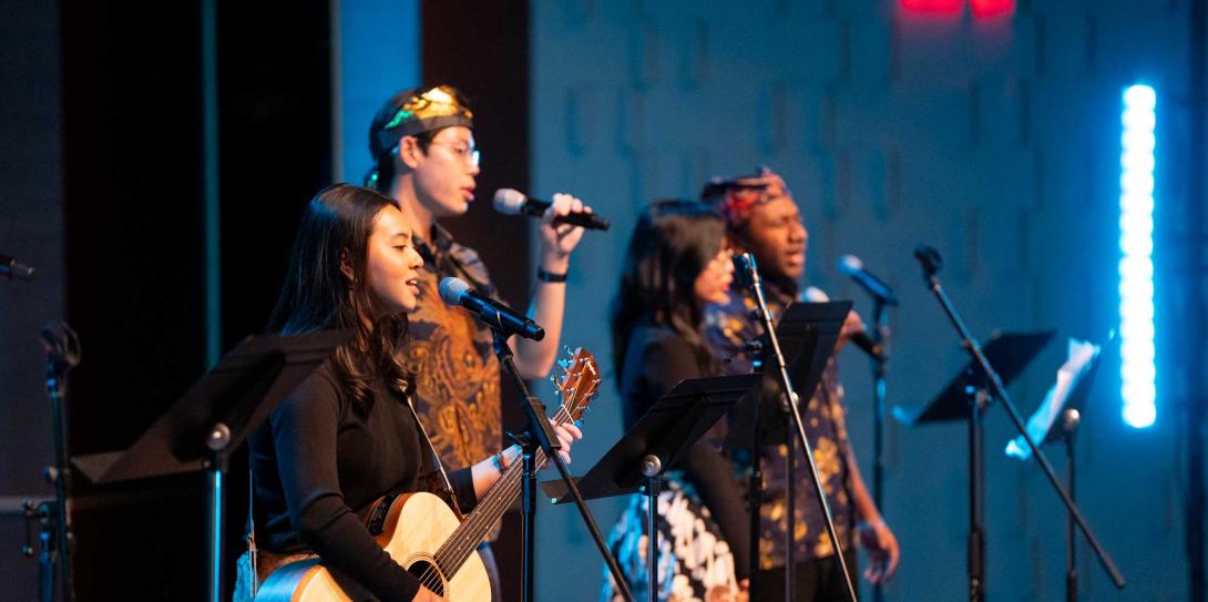 A diverse group of students leads worship with singing and guitar.