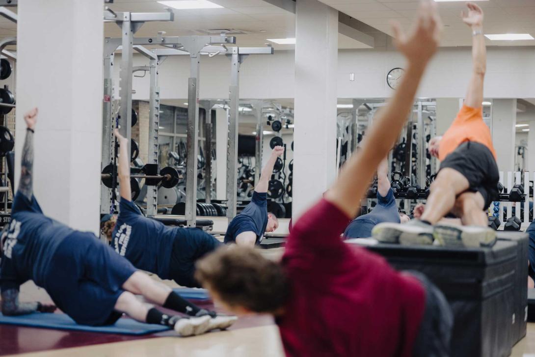A group of men and women stretch together in a weight room.