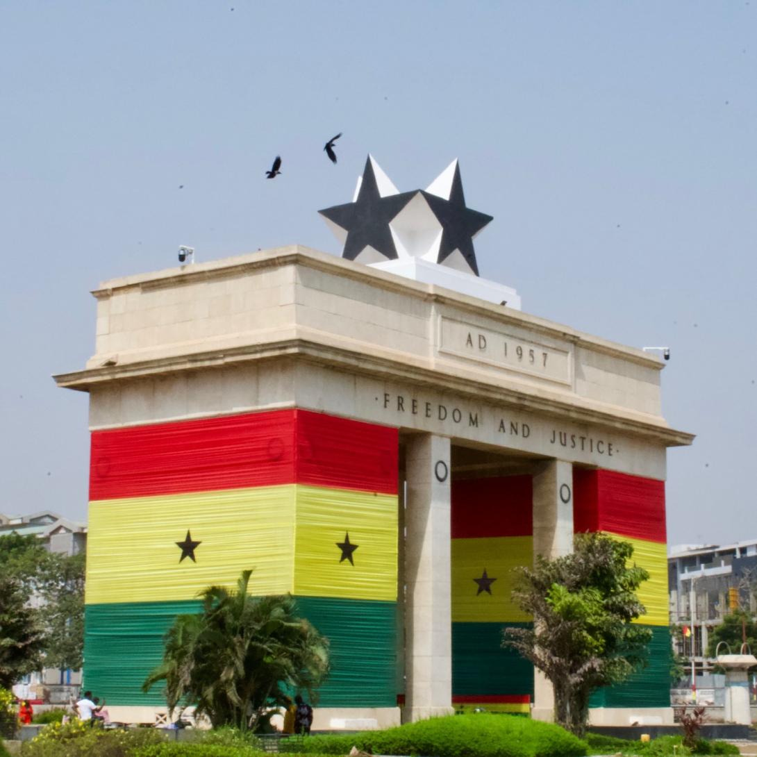 Image of a large concrete structure in Africa with red, yellow, and green stripes and two black stars on top with palm trees in the foreground