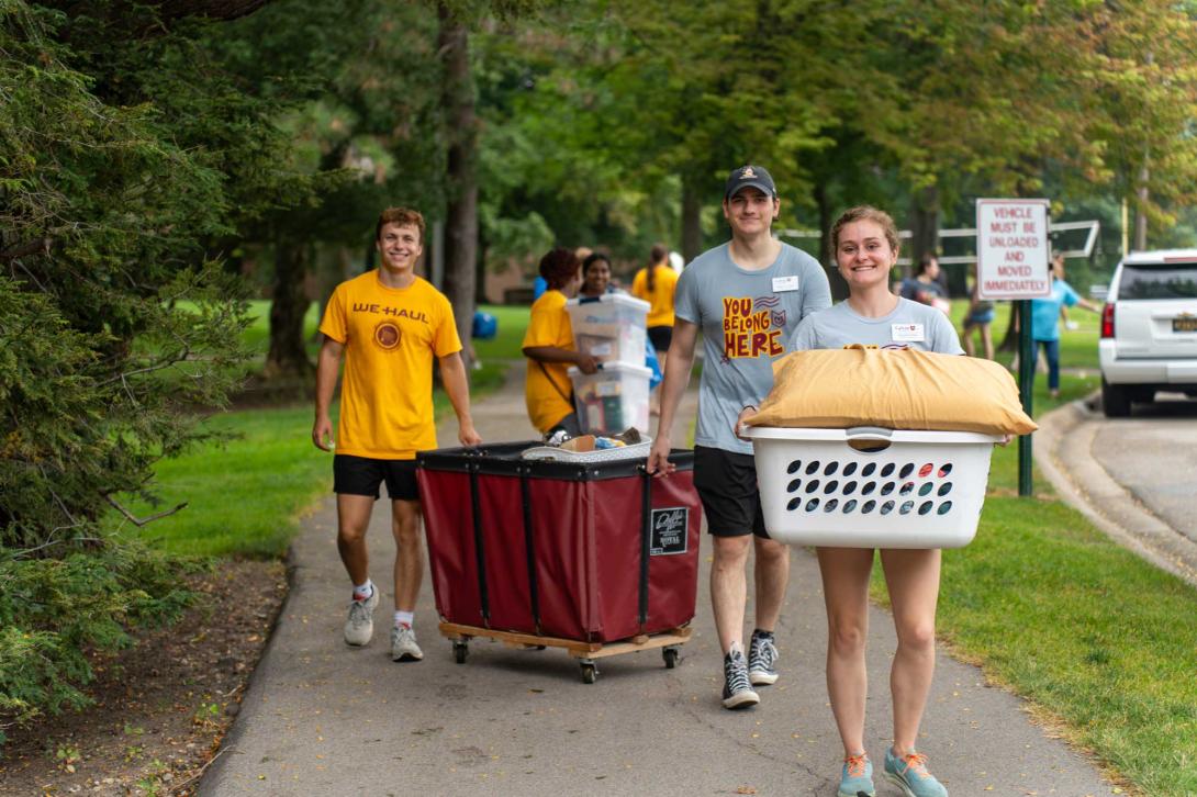 Calvin students wearing shirts that say We Haul and You Belong Here, carry carts and baskets full of belongings into the dorms.