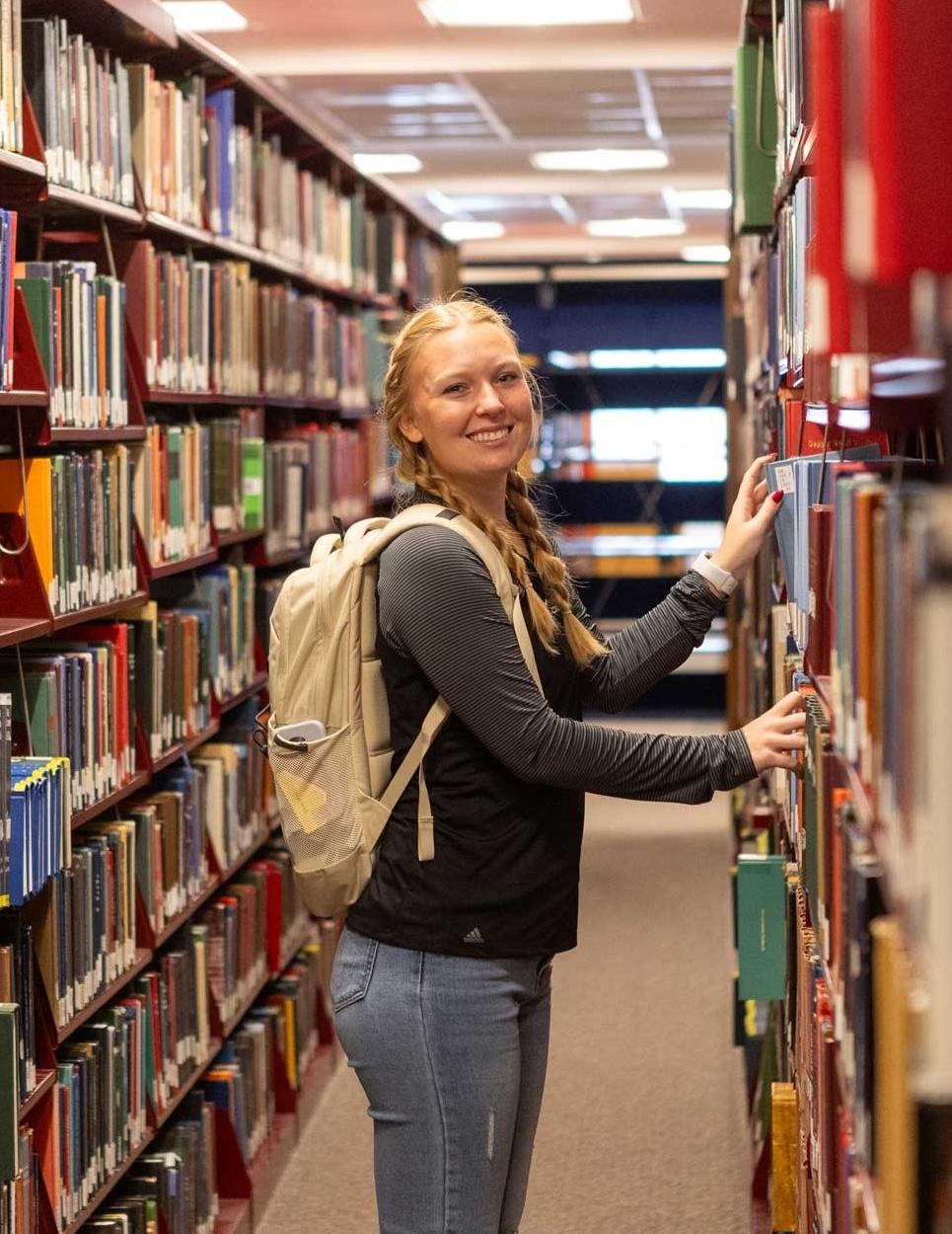 A student takes a book off the shelves at Calvin's Hekman Library.