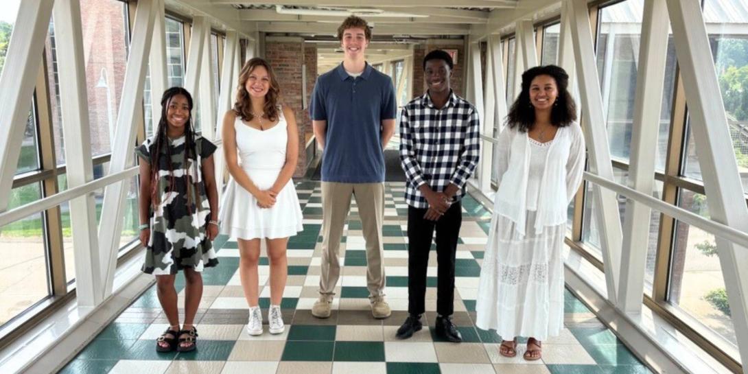 Five graduates from the Entrada Scholars program at Calvin University stand on the bridge connecting both sides of campus.