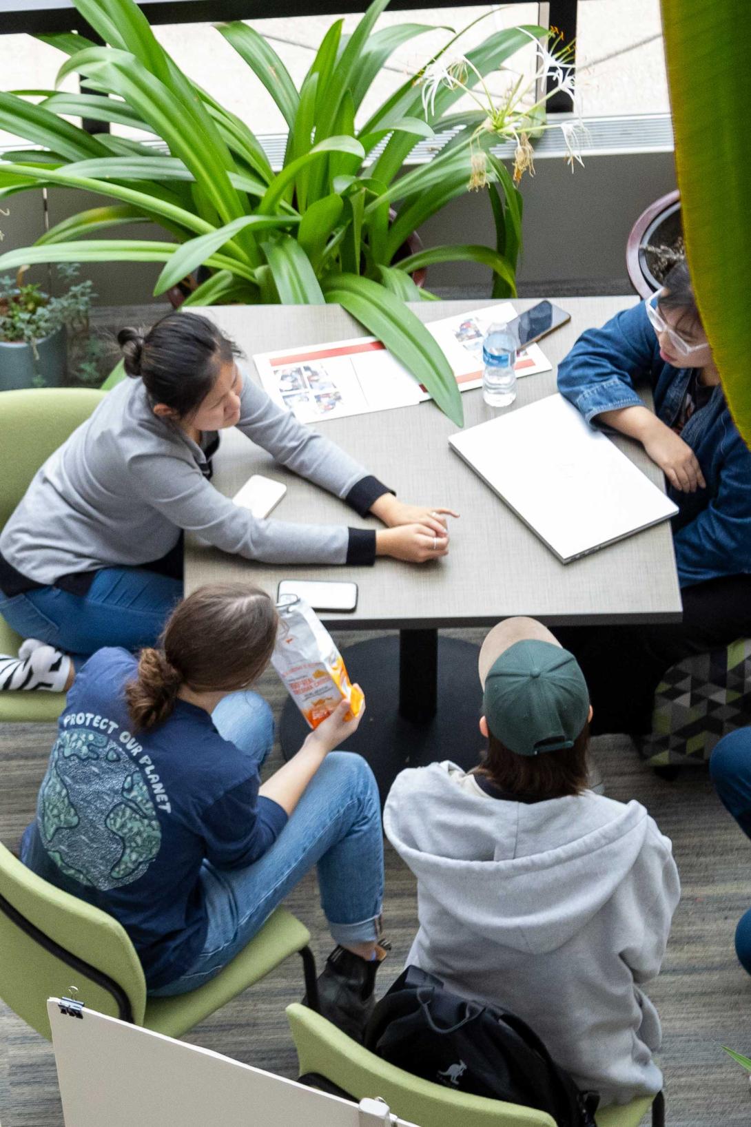 Students sit around a table doing research together, surrounded by green plants. 