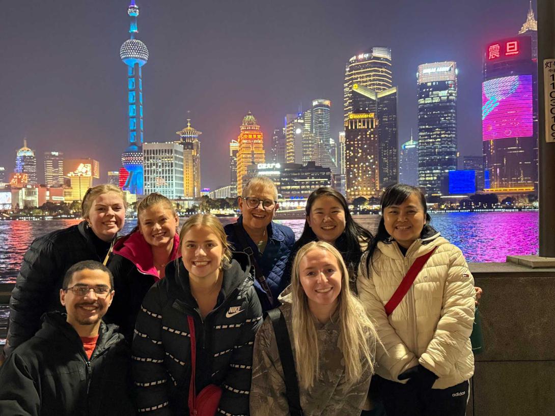 A group of students and professors in front of a city skyline in China, lit up at night.