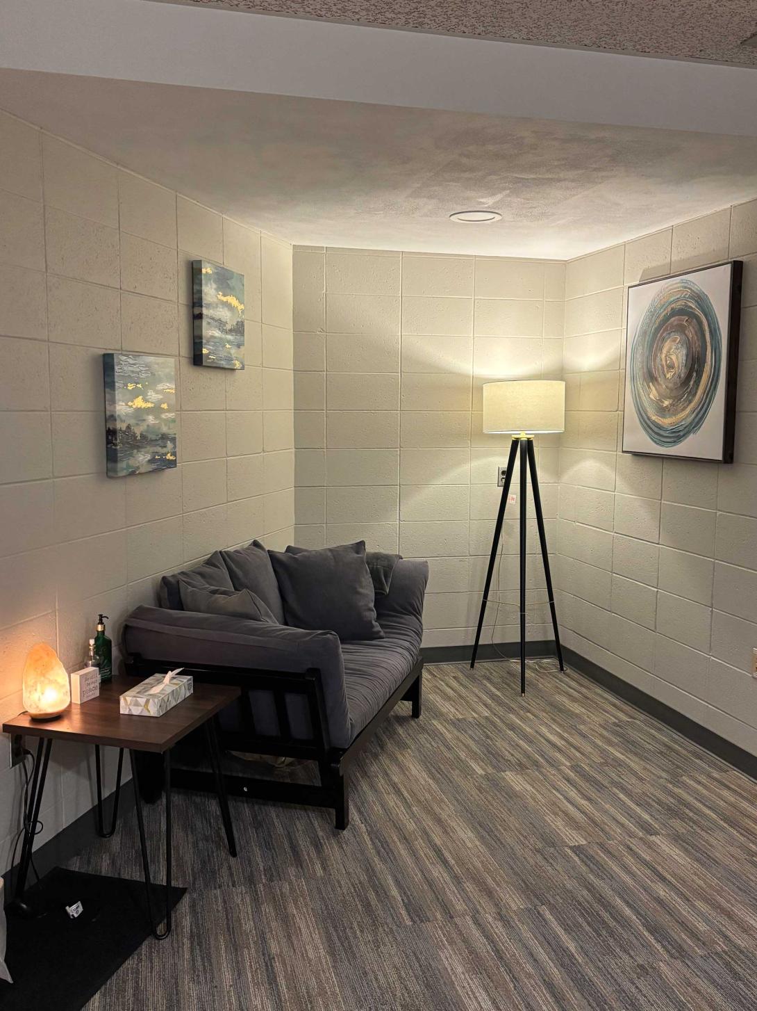 A room with a lamp, salt lamp, peaceful artwork, and sofa.