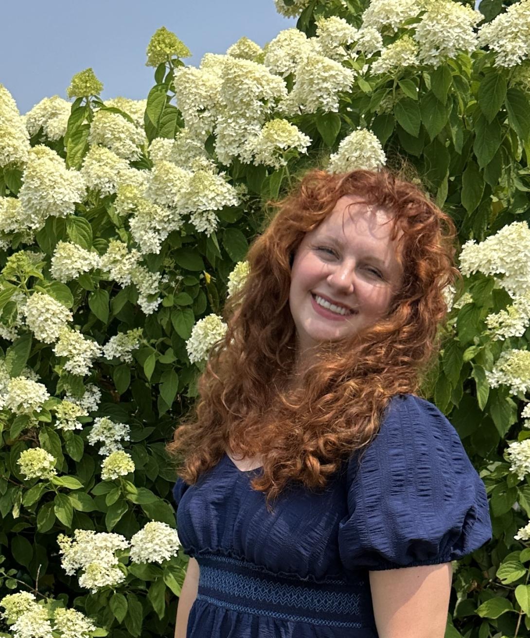 Jessi Galligan in a blue dress standing in front of hydrangea bushes in full bloom