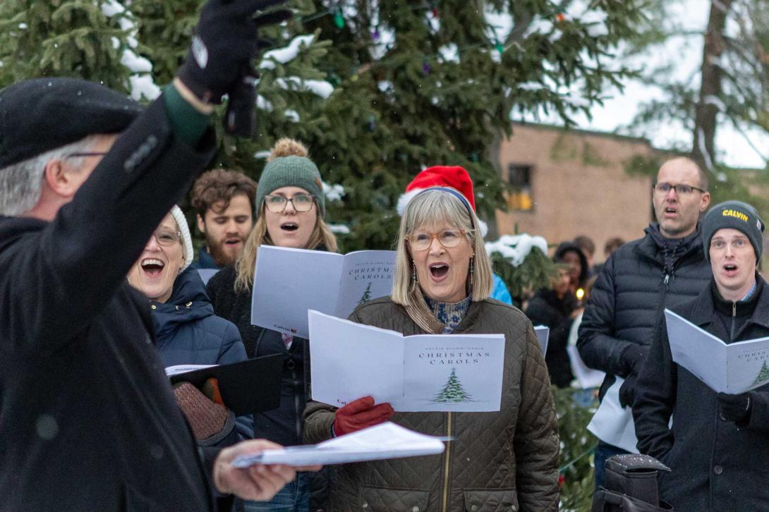 Calvin Alumni Choir members sing Christmas carols on the Calvin Commons Lawn, dressed in coats and hats for winter.