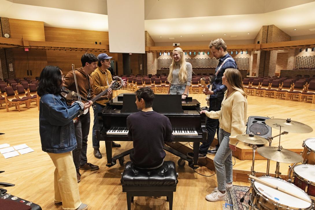 Music students gathered around a piano with their instruments.