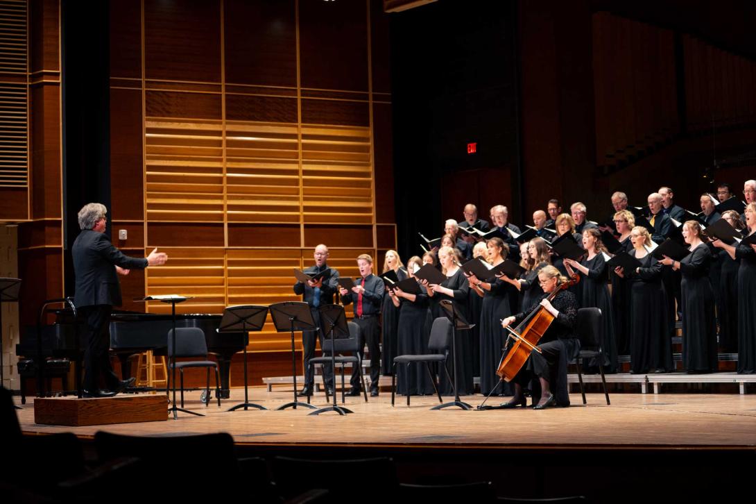 Sean Ivory conducts the Calvin Alumni Choir on the Covenant Fine Arts Center stage, accompanied by a cello.