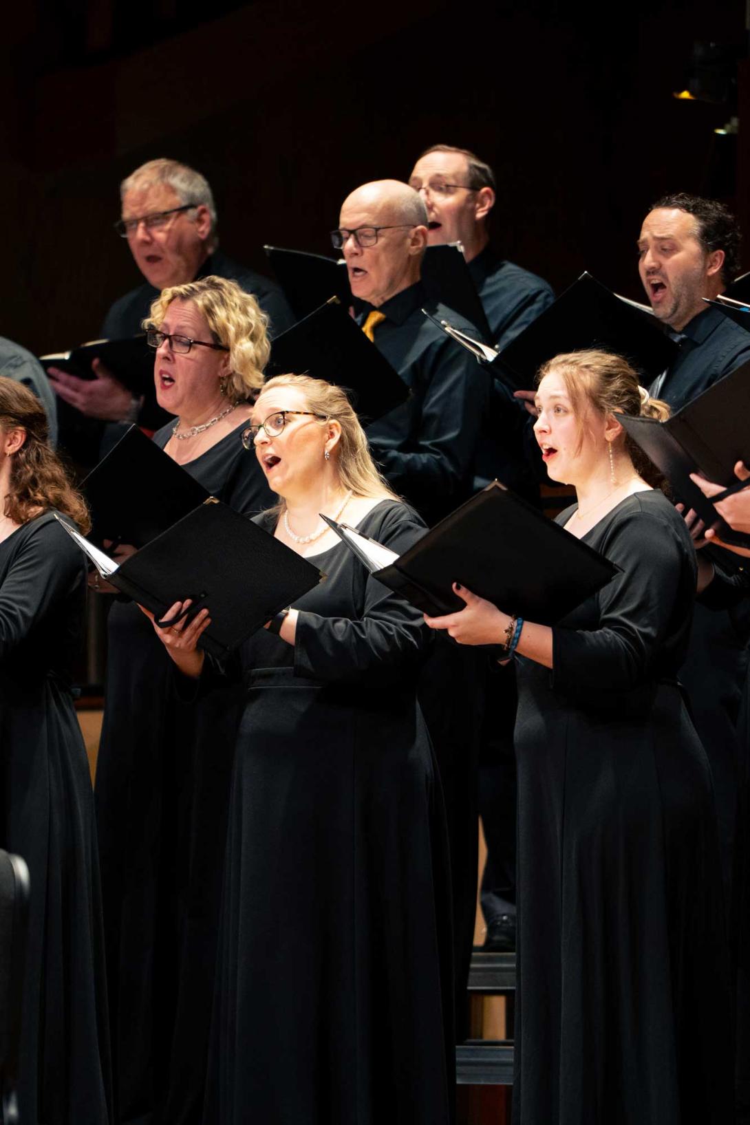 The Calvin Alumni Choir performs onstage, holding black folders and in black concert attire.