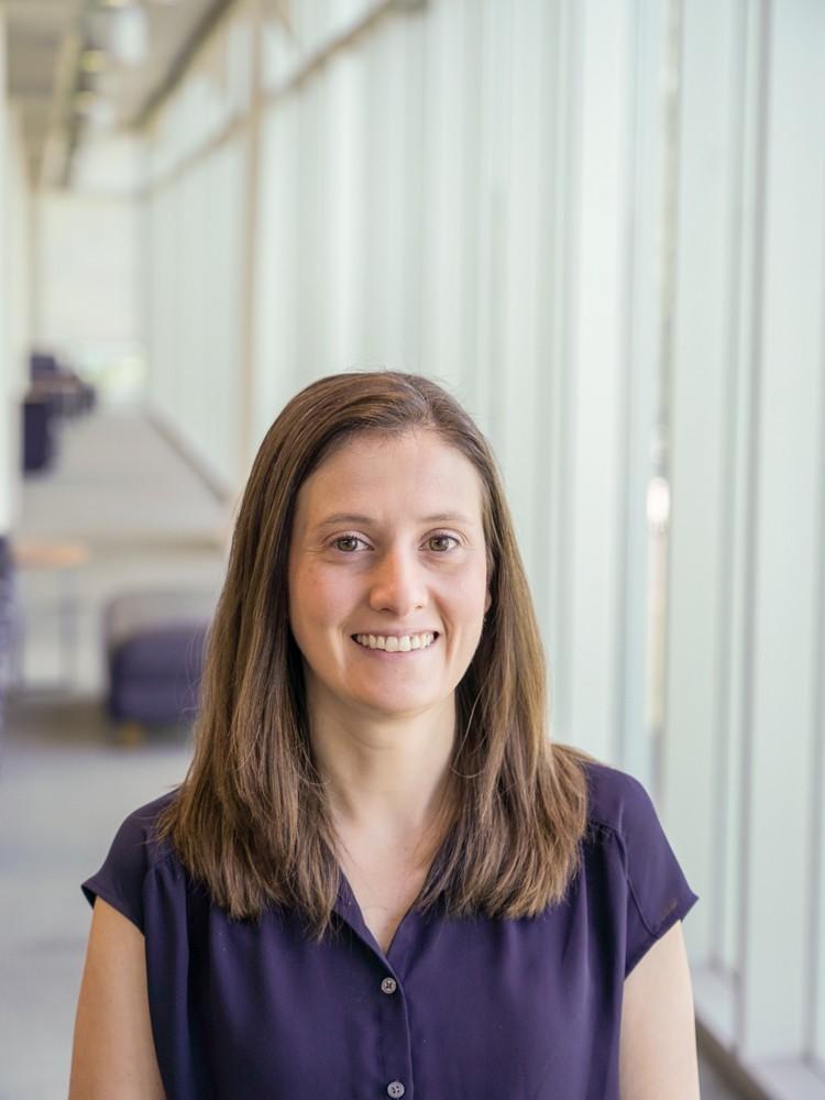 Jessica Thayer standing in a dark purple short-sleeved shirt with a blurred light background