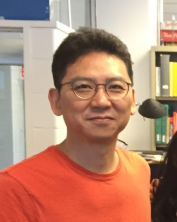 Junmo Cho looking at the camera - a man with glasses and an orange shirt