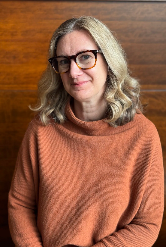 Photo of Kelli Scholten, smiling in front of brown wood background
