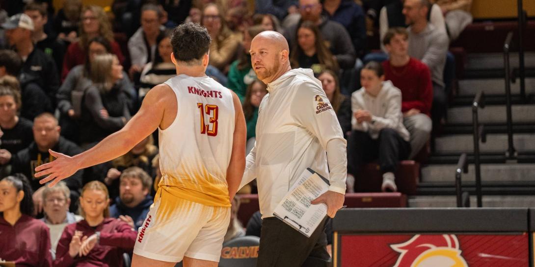 Aaron Sagraves walks the sideline with a Calvin men's volleyball player during a game.