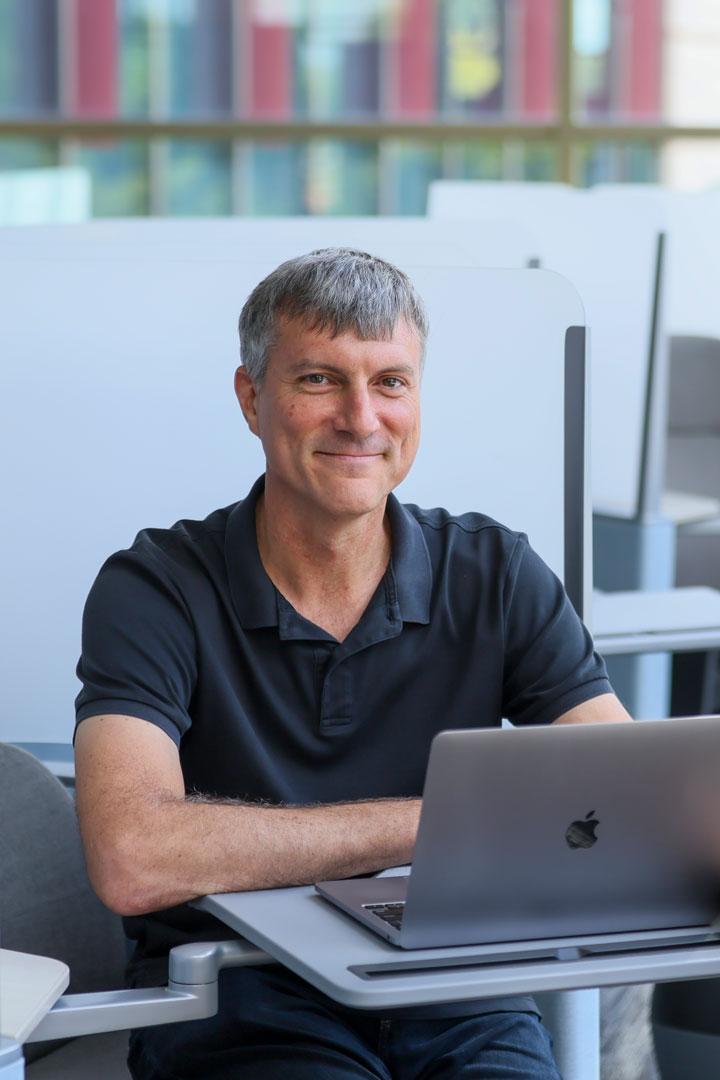 A middle-aged man sits with a laptop, working on courses for Calvin's MBA.