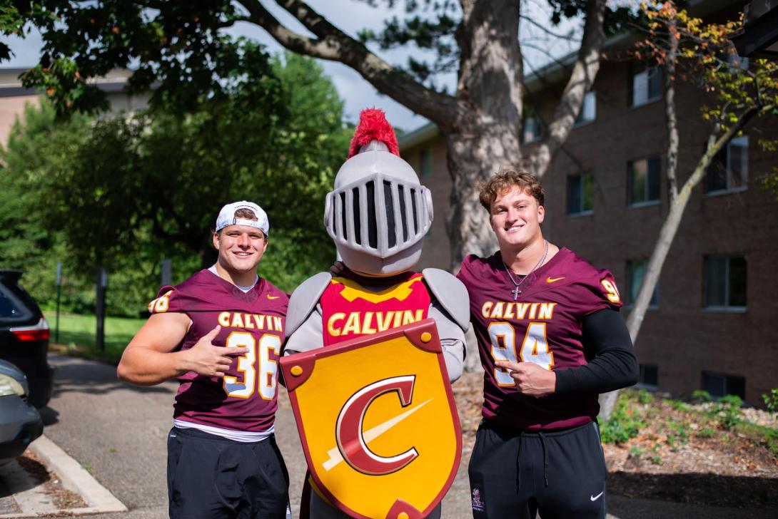 Joust, the Calvin knight mascot, poses with two Calvin football players giving thumbs up on move-in day.