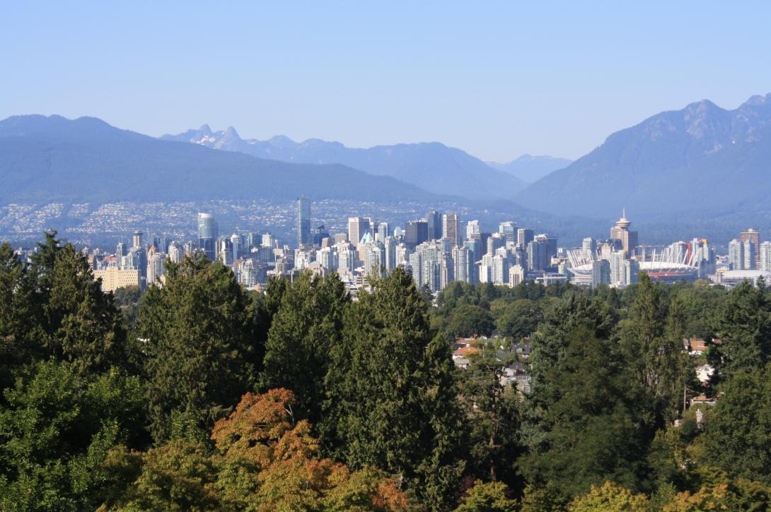 View of the Vancouver skyline, with forest in the foreground, and mountains in the distance.