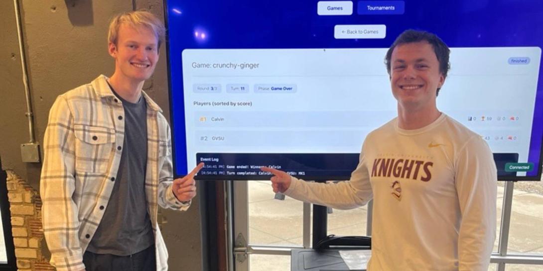 Nicholas Roberts and Benjamin Kosters point at a TV monitor