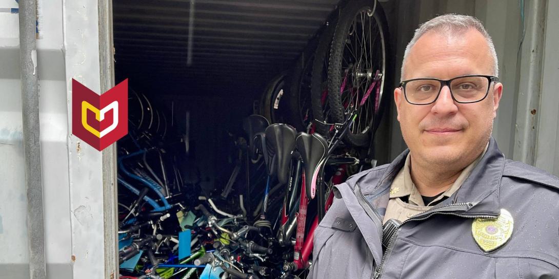 Tyson Moore stands in police uniform in front of stack of bikes