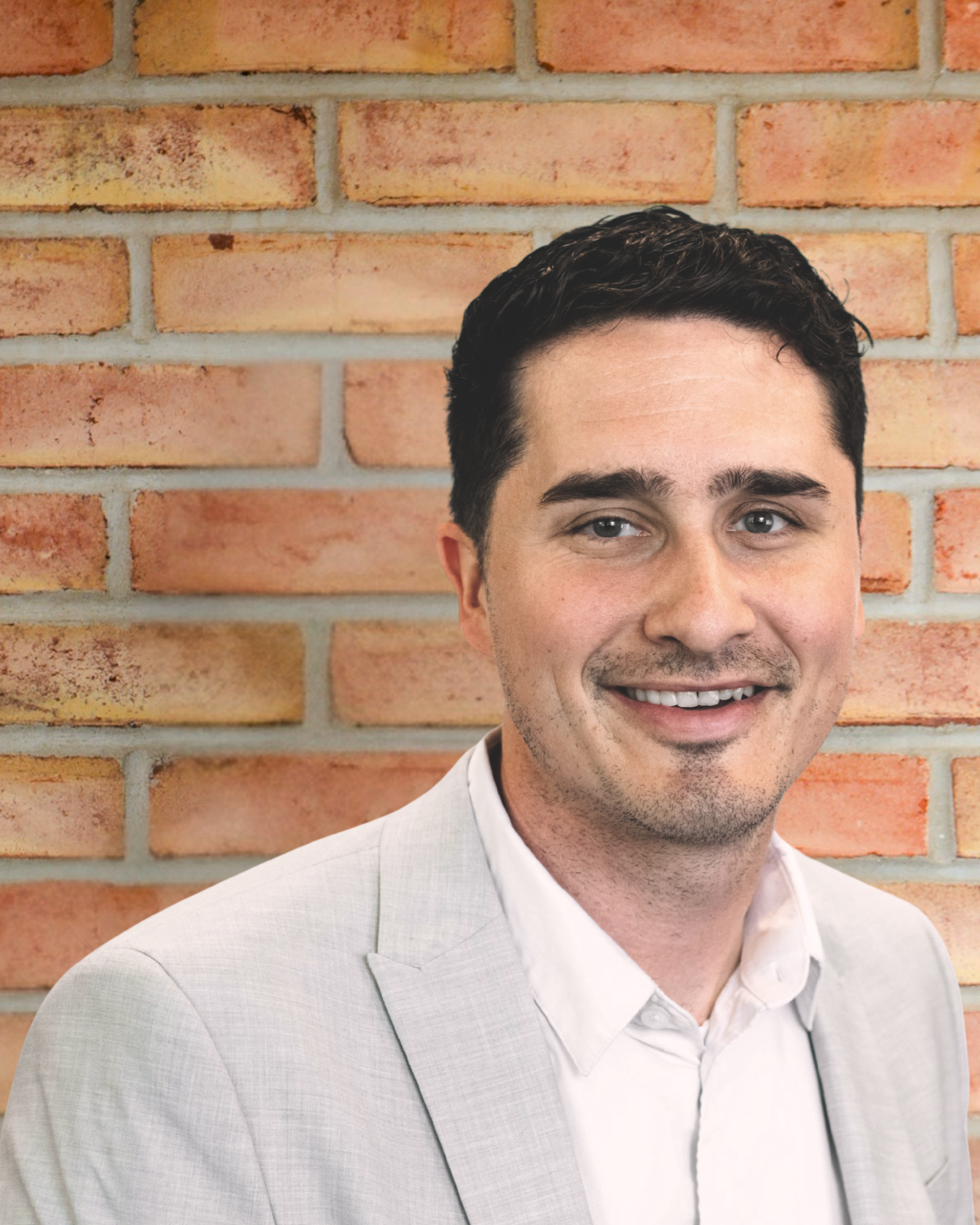 Man with black hair standing in front of a brick wall. 