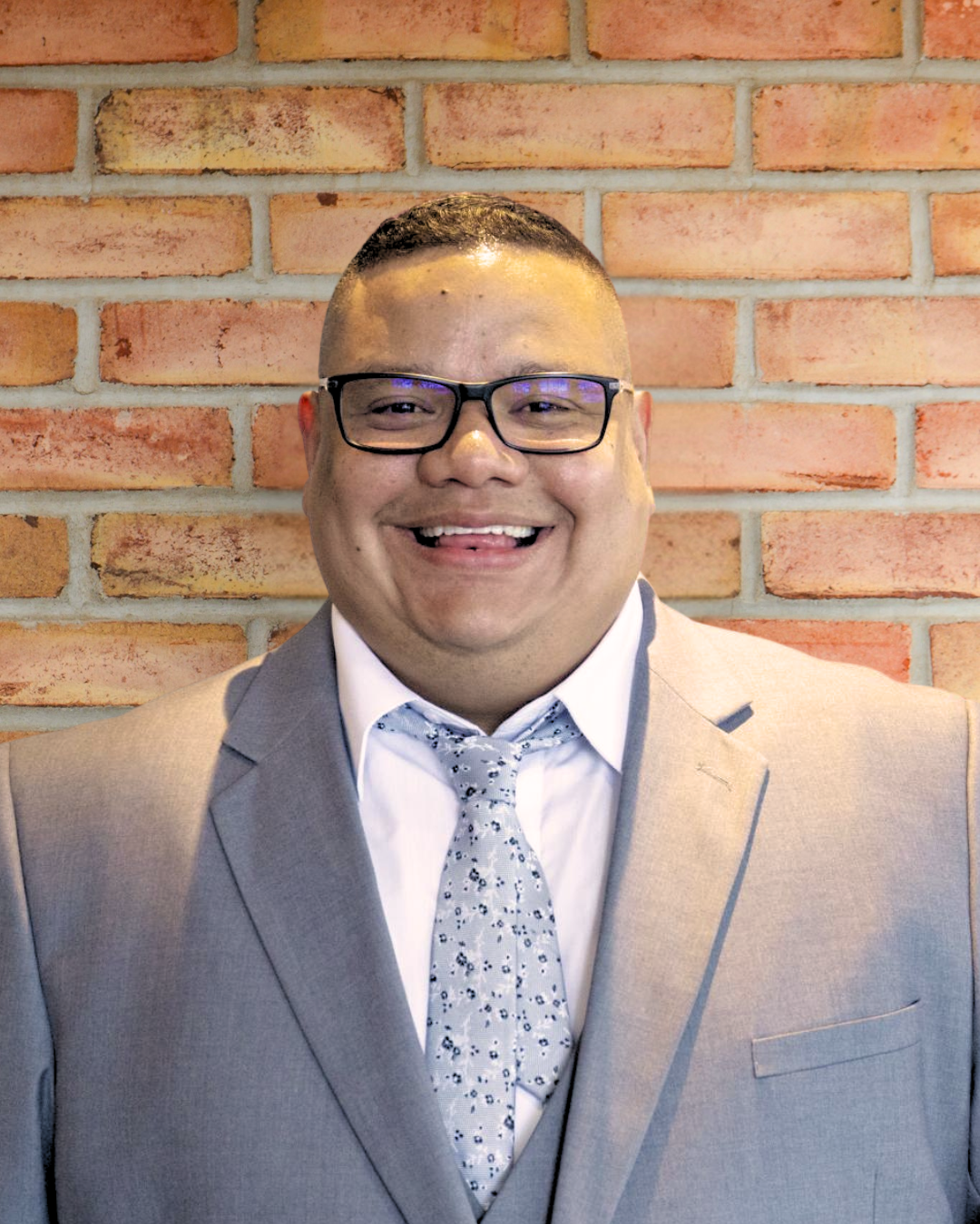 Man with glasses in front of brick wall. 