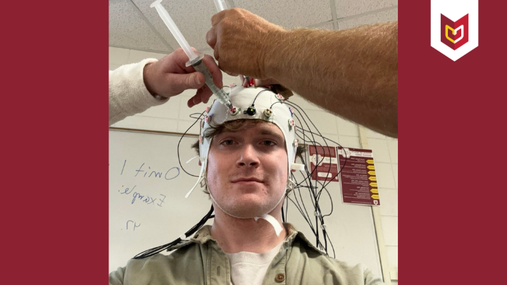 Luke Harlow with a cap with wires attached to it, supporting research at Calvin University.