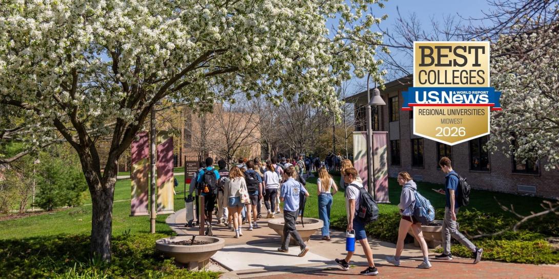 A path fills with students on Calvin's campus, under a blue sky with trees blooming for spring.