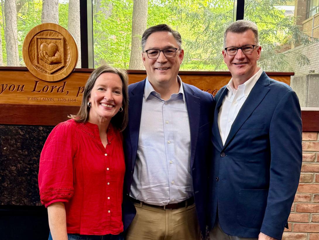 Becky Toly, Noah Toly, and Greg Elzinga stand together in front of the fireplace in Calvin's Spoelhof University Center.