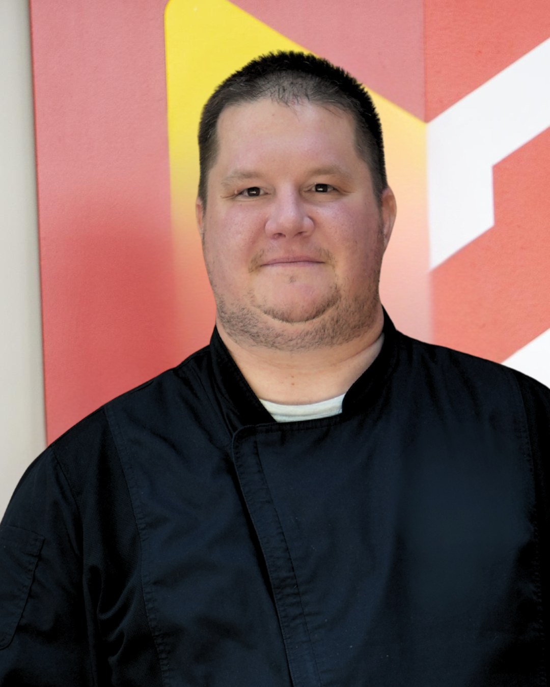 Man in with short brown hair in a Chef's coat. 