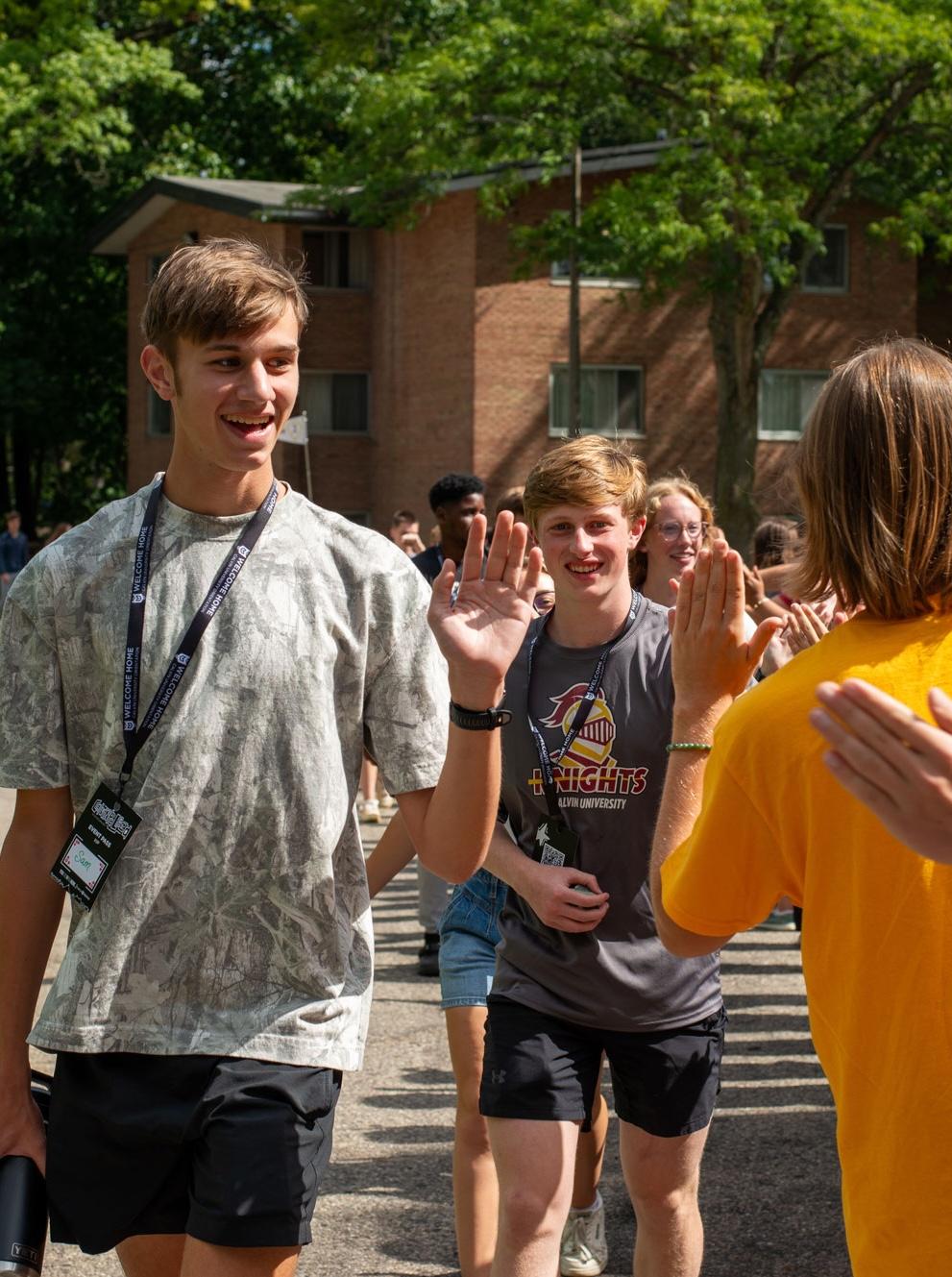New Calvin students with orientation lanyards get high fives from students lining the pathway.