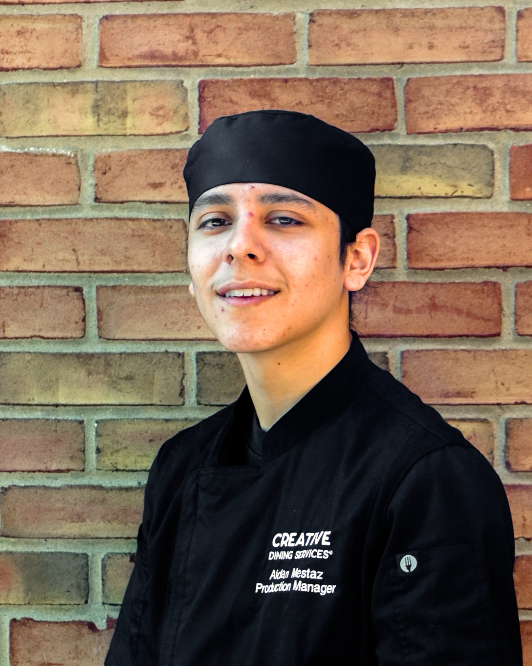 Man in a chef's hat in front of a brick wall.
