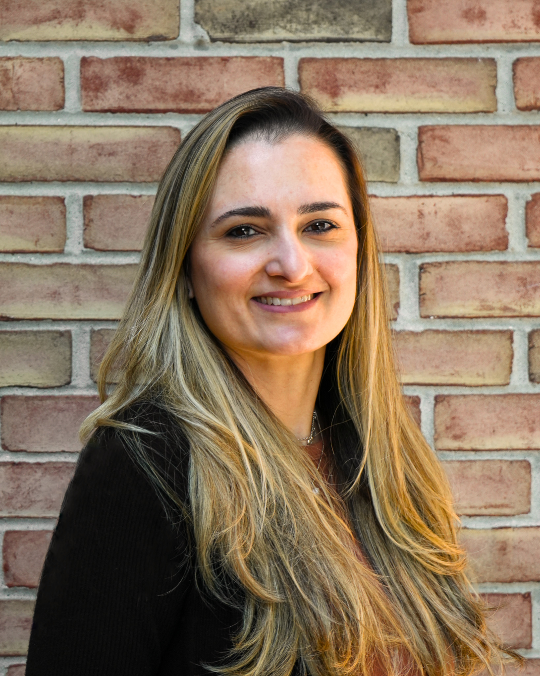 Woman with long light brown hair in front of a brick wall.