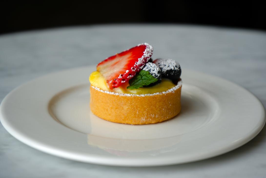 Tart on a plate with fresh berries, powdered sugar, and a mint leaf.