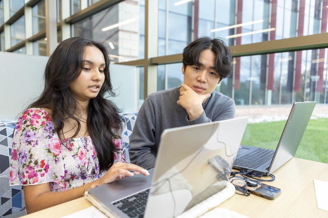 Two students sitting at a table looking at one of two laptops in front of them