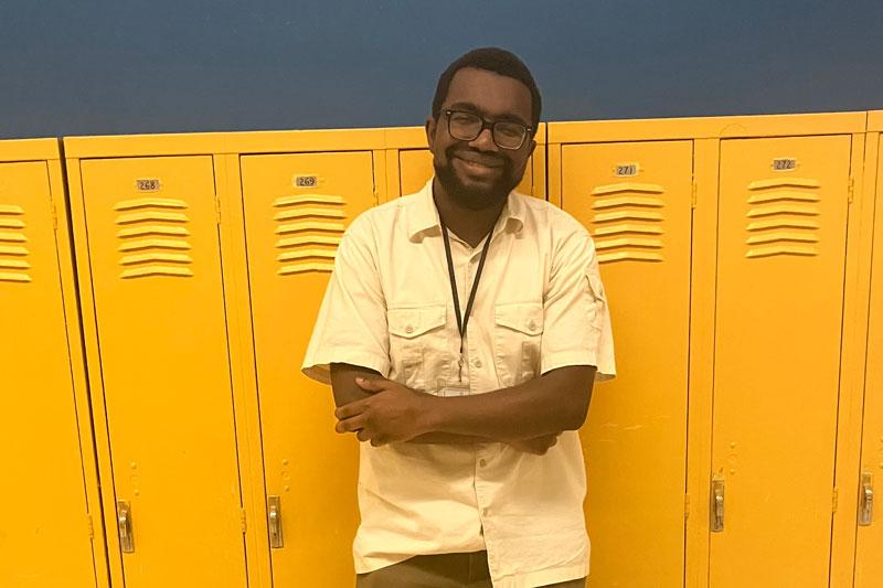 Noah Keen smiles with arms crossed in front of yellow lockers.