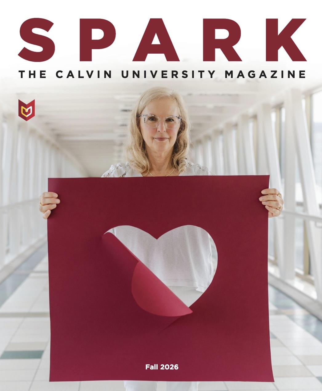 Julie Yonker, a Calvin professor, hold a large maroon poster with a heart cut out of it.
