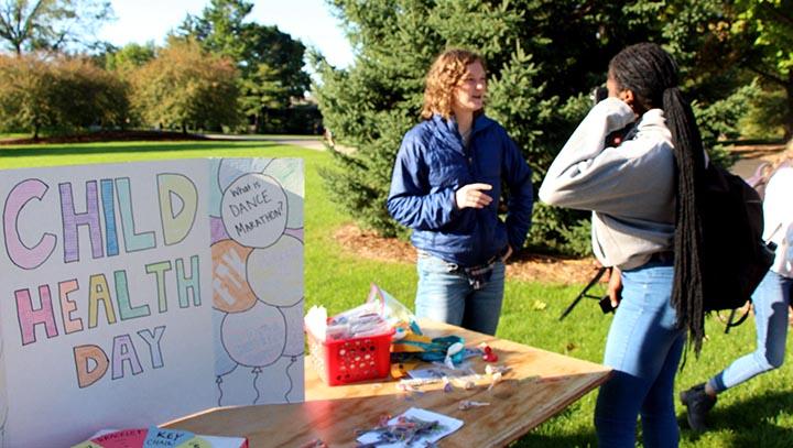 Two young people talk outside next to a table with a Child Health Day sign on it.