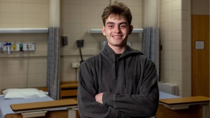 A male college student smiling wearing a sweatshirt in a hospital setting.