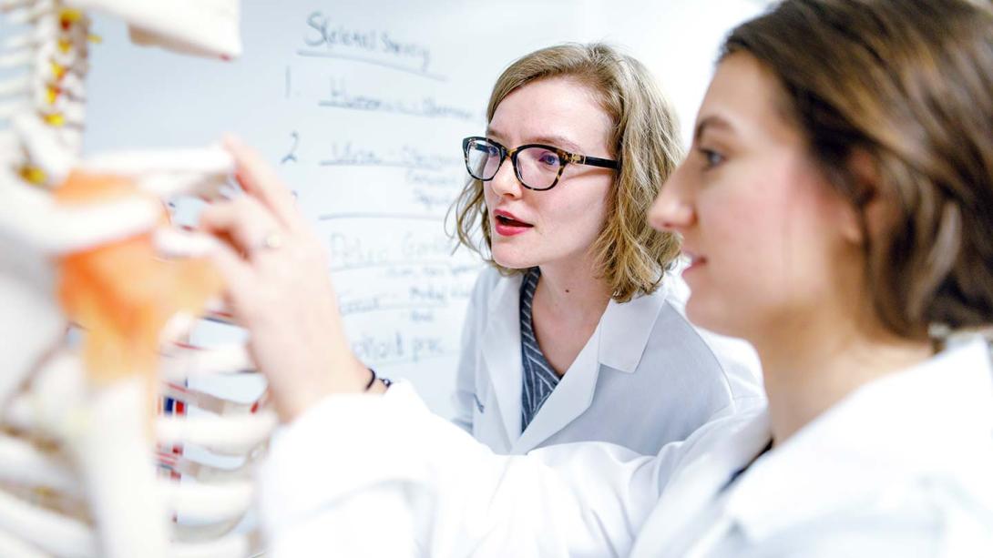 Students in white lab coats examining a skeleton