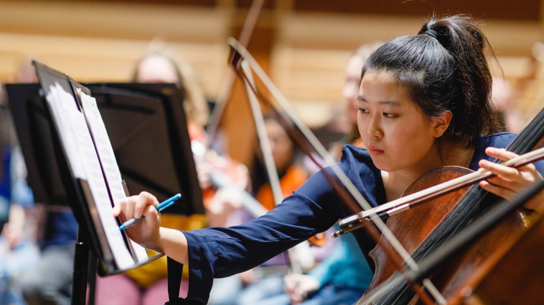 Cello player making a note on her sheet music.