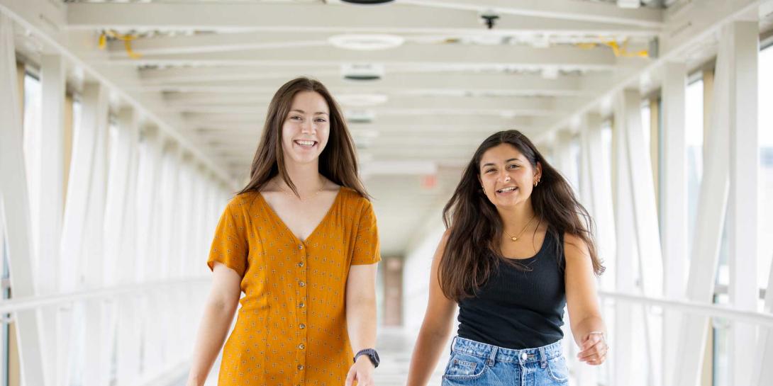 Two Calvin students walk across the overpass, smiling and walking toward the camera.