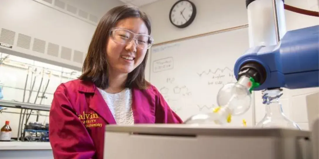 A student smiles as she performs research in a lab at Calvin University.