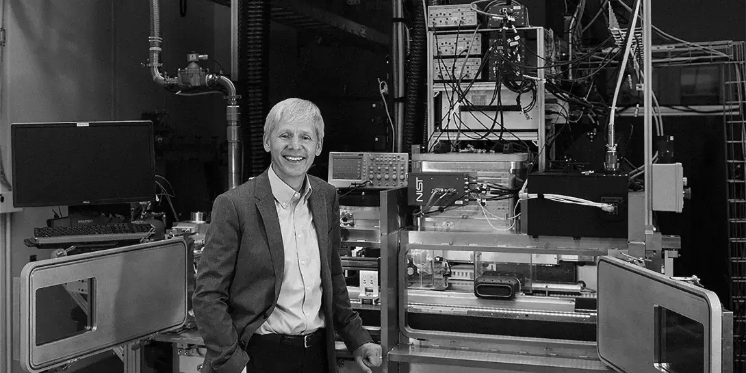 2024 Distinguished Alumni Award winner, Jim Olthoff, stands smiling in front of a scientific machine in his workplace