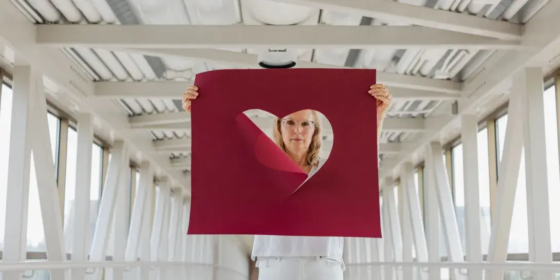 Julie Yonker, a Calvin professor, hold a large maroon poster with a heart cut out of it.